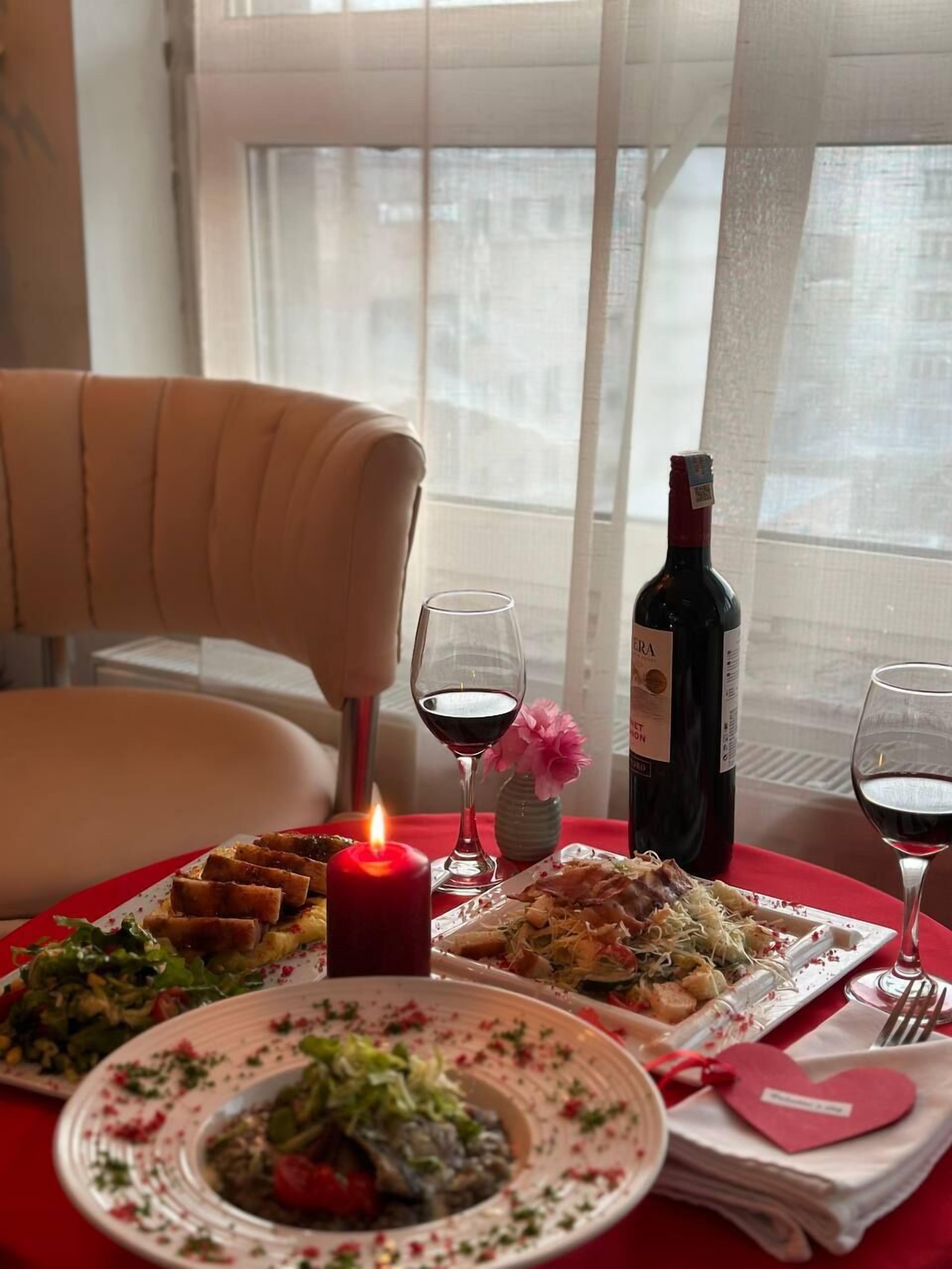 Una mesa de comedor servida con platos de comida, copas de vino, una vela y una botella de vino.