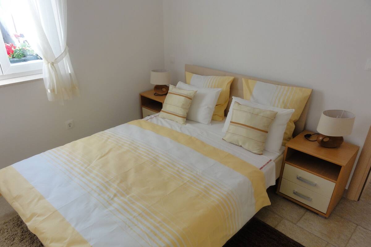 A neatly made bed with a striped bedspread, two bedside tables with lamps, and a window with curtains.