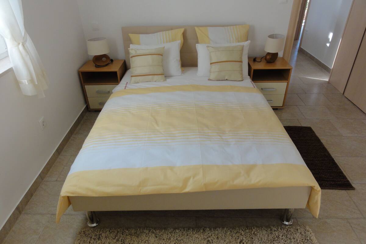 A neatly made bed with a striped bedspread, two bedside tables with lamps, and a rug on the floor.