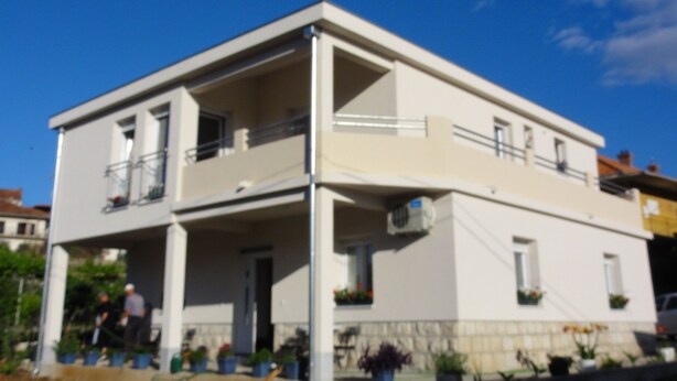 A two-story building with a balcony on the upper floor, a covered entrance, and potted plants around the exterior. - Apartments Cubela Beautiful Garden (Trogir)