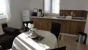 A compact kitchen with a refrigerator, microwave, and sink. There is a dining table with chairs and a vase of flowers. - Apartments Cubela Beautiful Garden (Trogir)