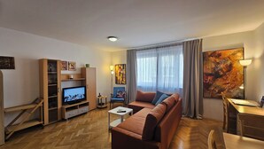 Un soggiorno con divano, televisore, mobiletto in legno e opere d'arte.