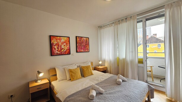Una camera d'albergo con un letto, due comodini con lampade, una finestra con tende e due elementi decorativi a parete.