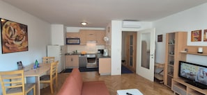 A compact living space with a kitchenette, a dining area, a sofa, and a TV.