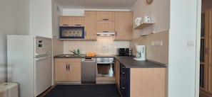 A compact kitchen with wooden cabinets, a dishwasher, an oven, a microwave, and a coffee maker.