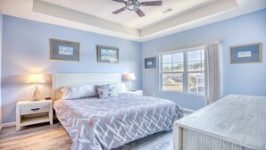 A bedroom with a bed, two bedside tables, a ceiling fan, and a window with a view of buildings.