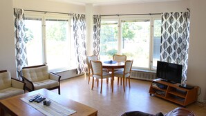 A living room with a dining table, chairs, a sofa, a TV, and a fireplace. - Liljeholmen Herrgård (Rimforsa)