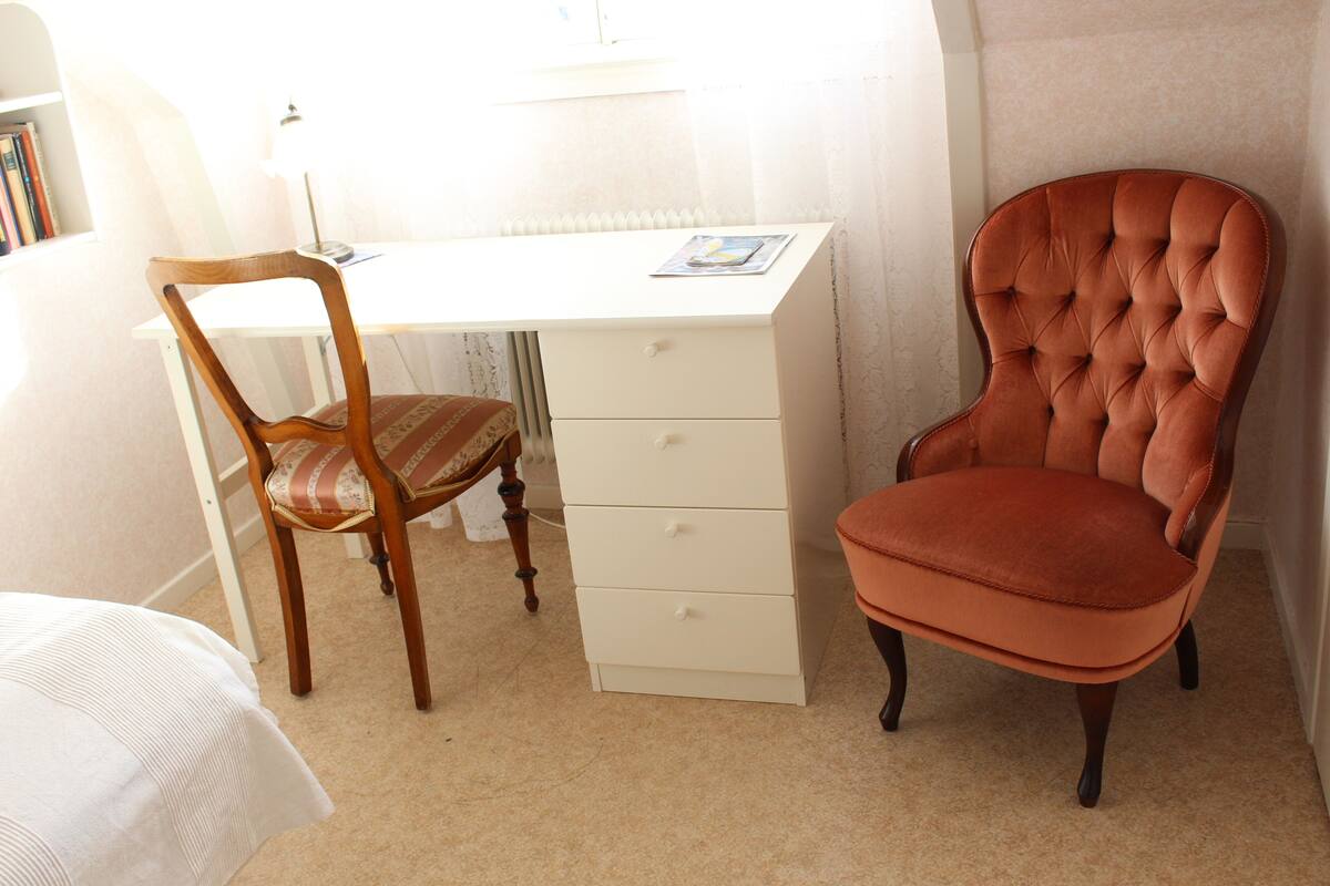 A study with a wooden chair, a cushioned armchair, and a white desk with drawers.
