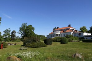 A large white building with a red roof, surrounded by greenery and a picnic area. - Liljeholmen Herrgård (Rimforsa)