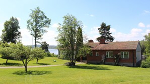 A house with a red roof, surrounded by green grass and trees, with a clear sky above. - Liljeholmen Herrgård (Rimforsa)