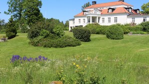 A large white building with a red roof, surrounded by lush green lawns and trees. - Liljeholmen Herrgård (Rimforsa)