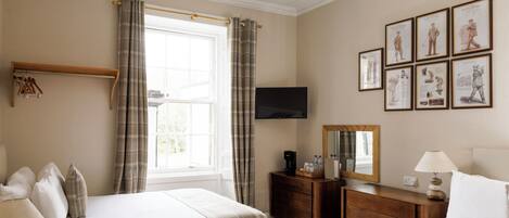 A hotel room with two beds, a desk, a chair, a dresser, a television, and framed pictures on the wall.