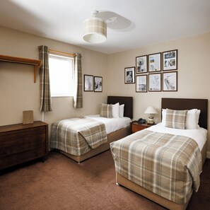 A hotel room with two beds, a wooden dresser, a bedside table with a lamp, a window with curtains, and framed pictures on the wall. - The Dunvegan Hotel (St. Andrews)