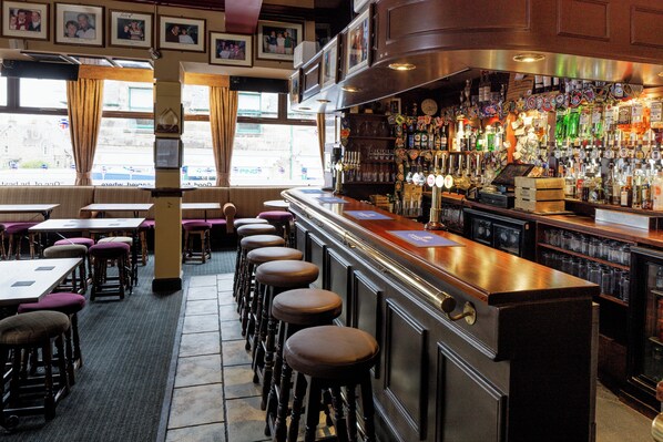 A bar area with stools, a bar counter, and shelves with bottles. - The Dunvegan Hotel (St. Andrews)