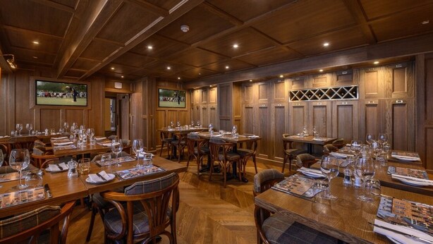 A conference room with wooden paneling, multiple tables set with wine glasses and menus, and a television screen displaying a sports event. - The Dunvegan Hotel (St. Andrews)