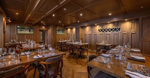 A conference room with wooden paneling, multiple tables set with wine glasses and menus, and a television screen displaying a sports event. - The Dunvegan Hotel (St. Andrews)
