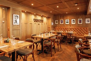 Un restaurante con paneles de madera, varias mesas para comer, sillas acolchadas y cuadros en las paredes.