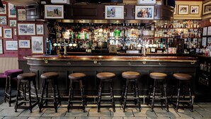A bar with a dark counter, multiple stools, and a variety of bottles and glasses. - The Dunvegan Hotel (St. Andrews)