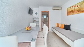 A modern living room with a white sofa, a dining table with chairs, and a TV mounted on the wall. - Apartment Lozovina - Panoramic Sea View (Seget)
