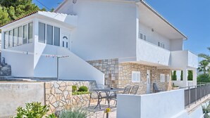 A two-story building with a stone facade, a balcony, and a patio area with outdoor seating. - Apartment Lozovina - Panoramic Sea View (Seget)