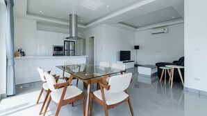A modern kitchen with white cabinets, stainless steel appliances, and a glass dining table with white chairs. - Orchid Paradise Homes OPV420 (Hua Hin)