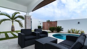 A patio area with dark wicker furniture, a swimming pool, and a stone pillar. - Orchid Paradise Homes OPV420 (Hua Hin)