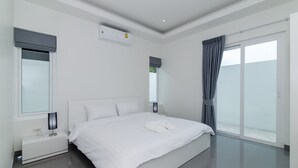 A modern bedroom with a large bed, a nightstand, a wall-mounted air conditioner, and a sliding glass door to the outside. - Orchid Paradise Homes OPV420 (Hua Hin)