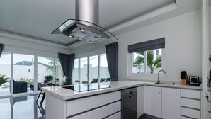 A modern kitchen with a central island, built-in dishwasher, and a large window with a view of the outdoors. - Orchid Paradise Homes OPV420 (Hua Hin)