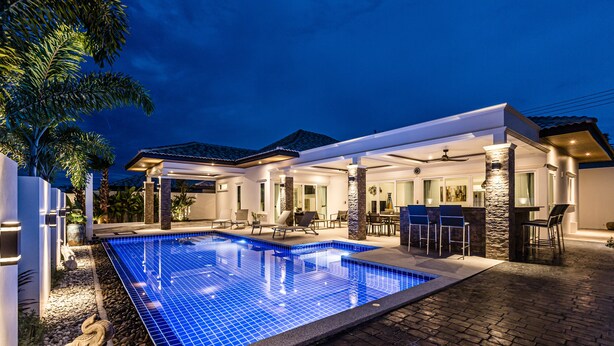 Une piscine avec une terrasse carrelée, un patio couvert et un pilier en pierre.