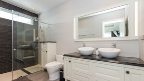 Une salle de bain moderne avec une douche à parois de verre, des toilettes blanches et un meuble-lavabo double avec un grand miroir au-dessus.