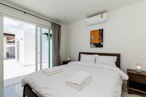 Habitación de hotel moderna con una cama grande, una mesita de noche con lámpara, aire acondicionado instalado en la pared y vistas al balcón exterior.