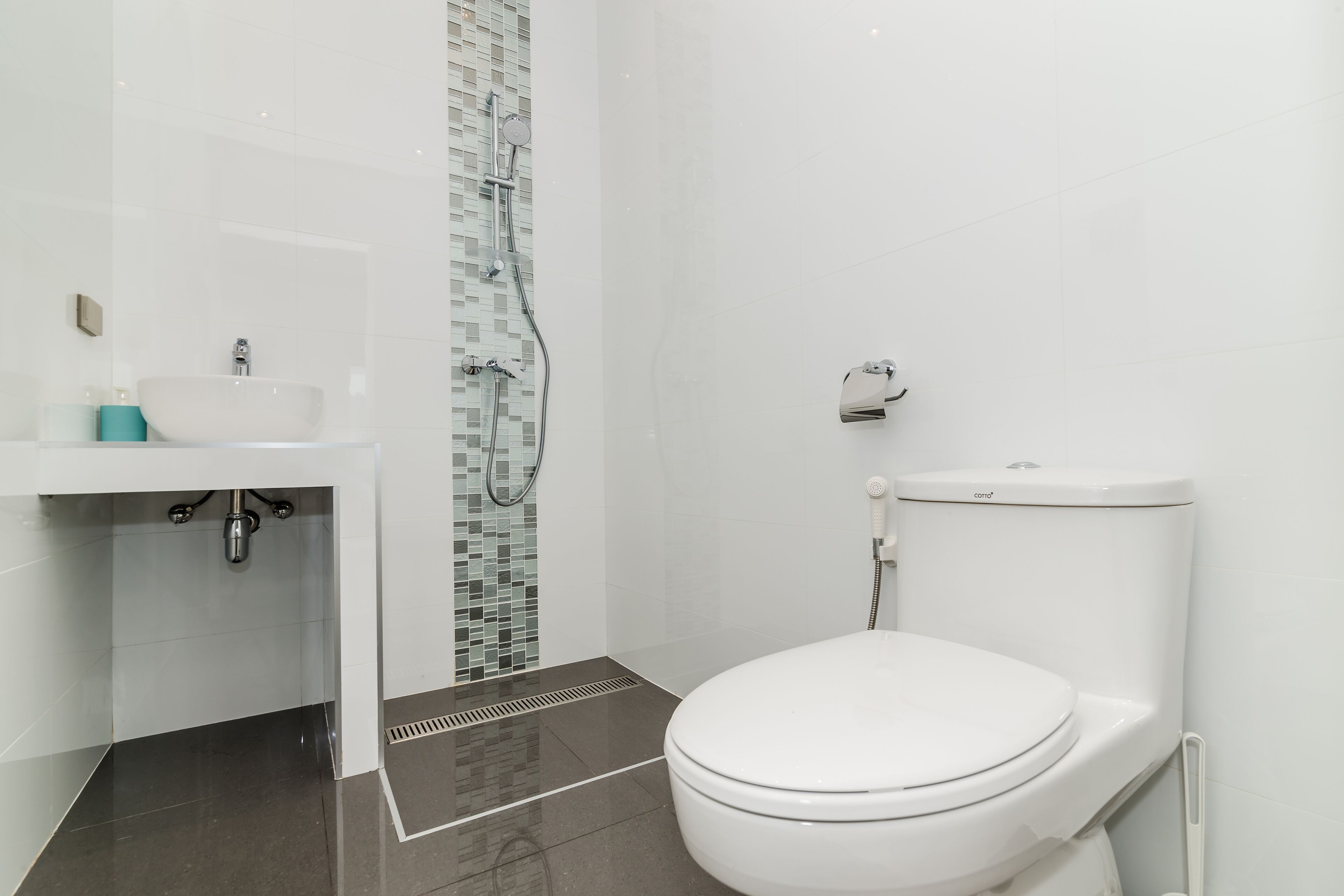 A modern bathroom with a white sink, a toilet, and a shower area.