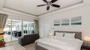 A modern hotel room with a large bed, a ceiling fan, and a view of the outdoor area through glass doors. - Orchid Paradise Homes OPV313 (Hua Hin)