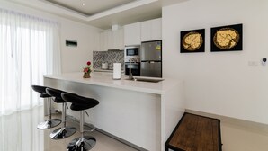 A modern kitchen with white cabinets, stainless steel appliances, and a bar area with black stools. - Orchid Paradise Homes OPV313 (Hua Hin)