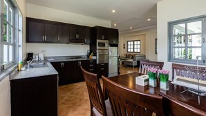 Una cocina moderna con armarios oscuros, horno empotrado y comedor con sillas y mesa de madera.