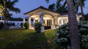 Una casa moderna con un porche cubierto, piscina y abundante vegetación.