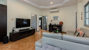 Una sala de estar moderna con un televisor de pantalla plana grande, mueble de entretenimiento de madera oscura, sofá de color gris claro y piso de baldosas.