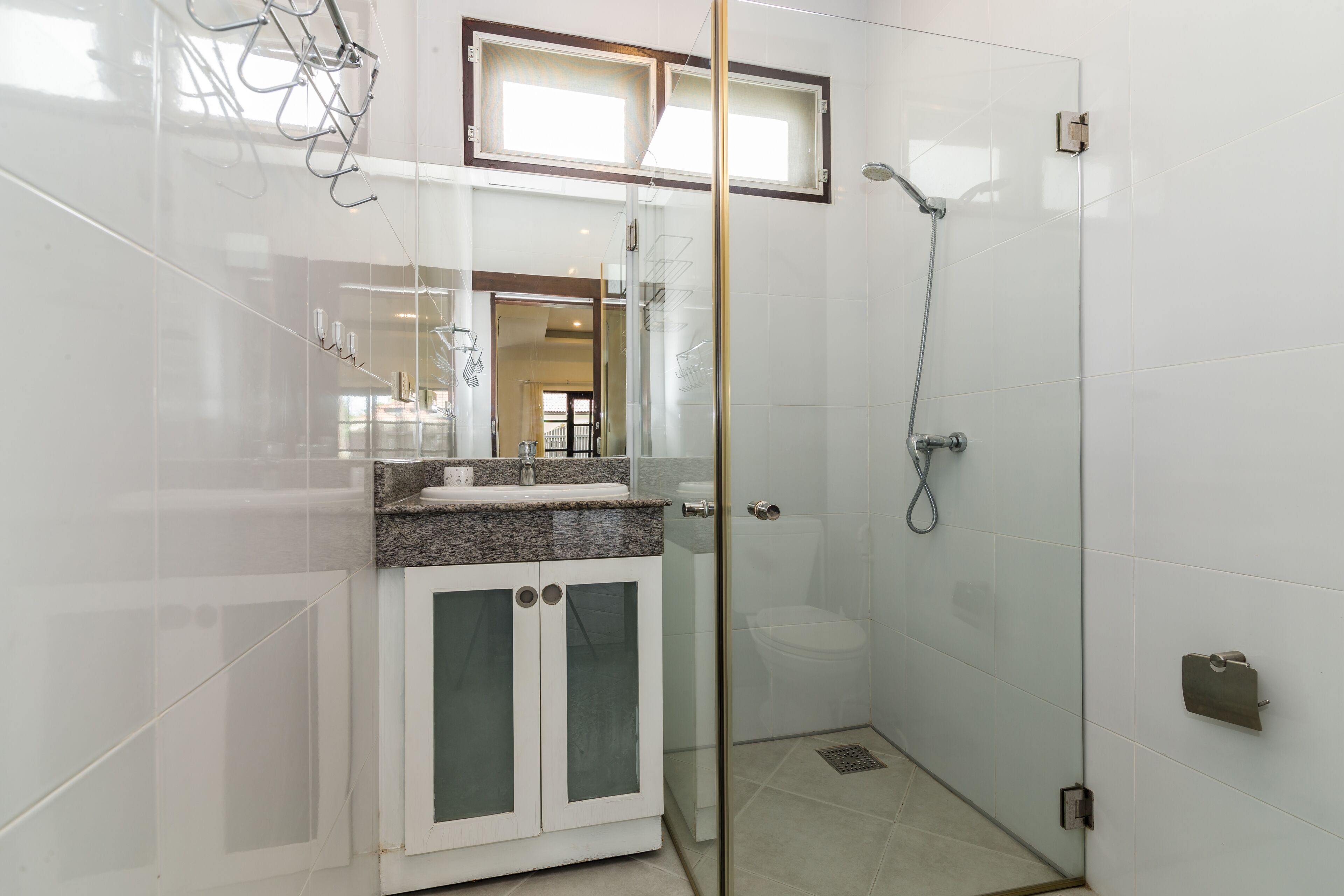 A modern bathroom with a glass shower enclosure, a granite countertop, and a white tiled floor.