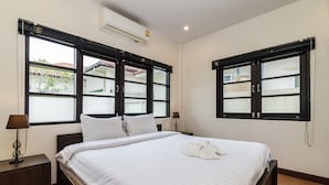 A neatly made bed with white linens, two bedside tables with lamps, and large windows with black frames. - Orchid Paradise Homes OPV22 (Hua Hin)
