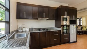 A modern kitchen with dark wood cabinets, stainless steel appliances, and a granite countertop. - Orchid Paradise Homes OPV22 (Hua Hin)