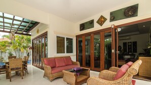 A spacious living area with wicker furniture, a glass coffee table, and a view of the outdoors.
