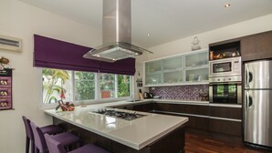 A modern kitchen with a central island, bar stools, stainless steel appliances, and a view of the outdoors.