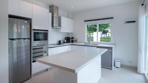 Une cuisine moderne dotée d’appareils électroménagers en acier inoxydable, d’un grand îlot central et d’une fenêtre offrant une vue sur la verdure environnante.