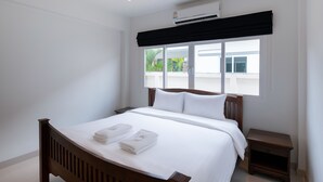 Un lit bien fait, avec du linge de lit et des serviettes blanches, un ventilateur de plafond, un appareil de climatisation et une fenêtre donnant sur un paysage verdoyant.