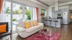 A modern living room with a sofa, a glass coffee table, and a view of a pool.