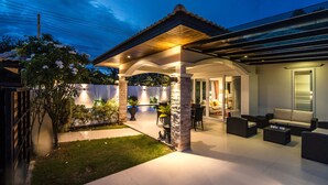 A covered outdoor patio with a pool, seating area, and a well-lit entrance.