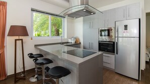 A modern kitchen with a central island, bar stools, a built-in oven, and a refrigerator.