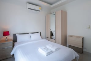 A neatly made bed with white linens and towels, a bedside lamp, a wardrobe, and a small bedside table.