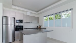 A modern kitchen with stainless steel appliances, a central island, and a large window providing natural light. - Orchid Paradise Homes OPV401 (Hua Hin)