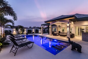 Une maison moderne dotée d’une piscine, d’un espace salon extérieur et d’un pilier en pierre.